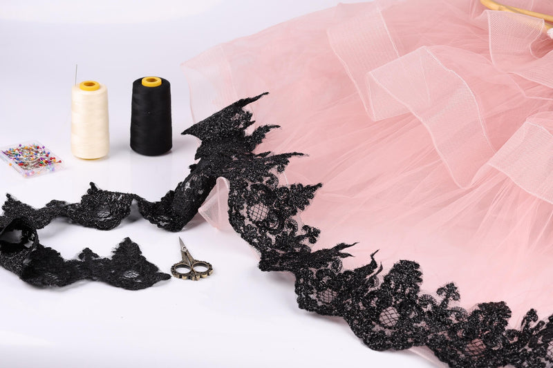 sewing supplies, including two spools of thread, a pair of scissors, and a pink tulle skirt with black lace trim.