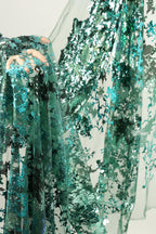 a close-up view of a fabric with a green and blue floral pattern, with a hand visible in the top right corner.