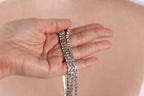 A hand holding a silver necklace with multiple strands of sparkling rhinestones.