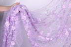 A hand is holding a piece of fabric with a delicate floral pattern in shades of purple.
