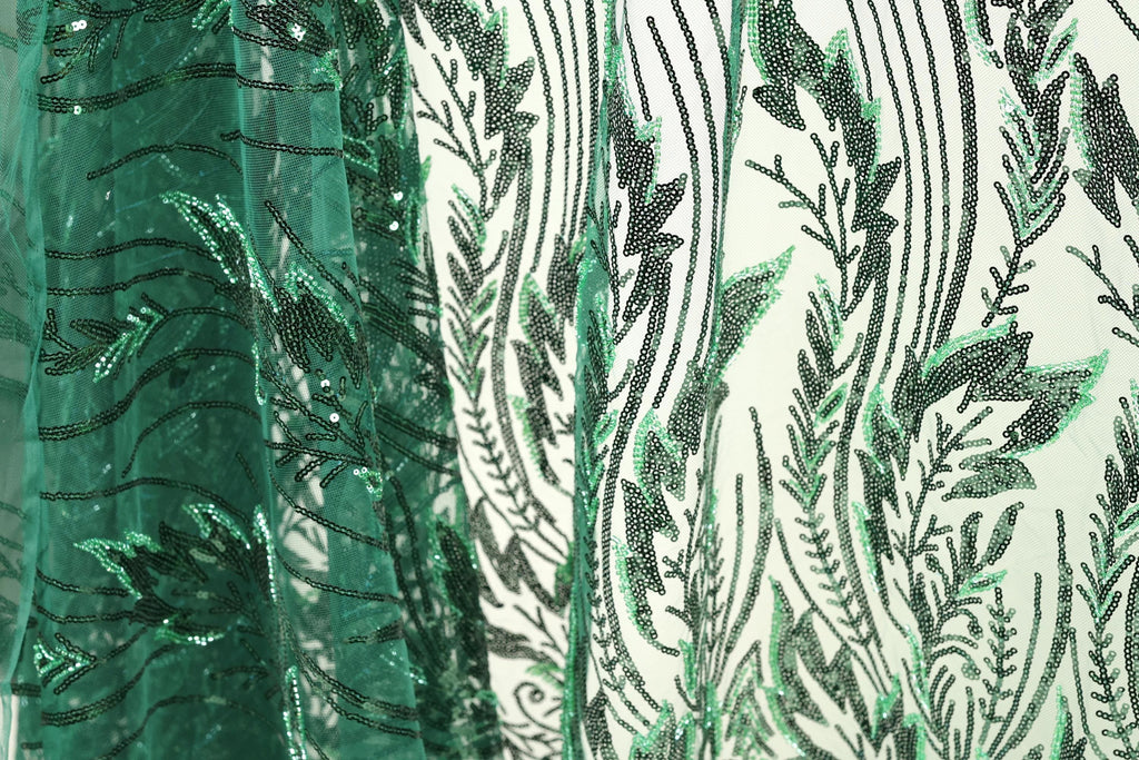a close-up view of a fabric with a green and black leaf pattern. The fabric appears to be made of a sheer material, with a repeating pattern of green leaves and black lines. The leaves are arranged in a vertical orientation, creating a sense of depth and texture in the image.