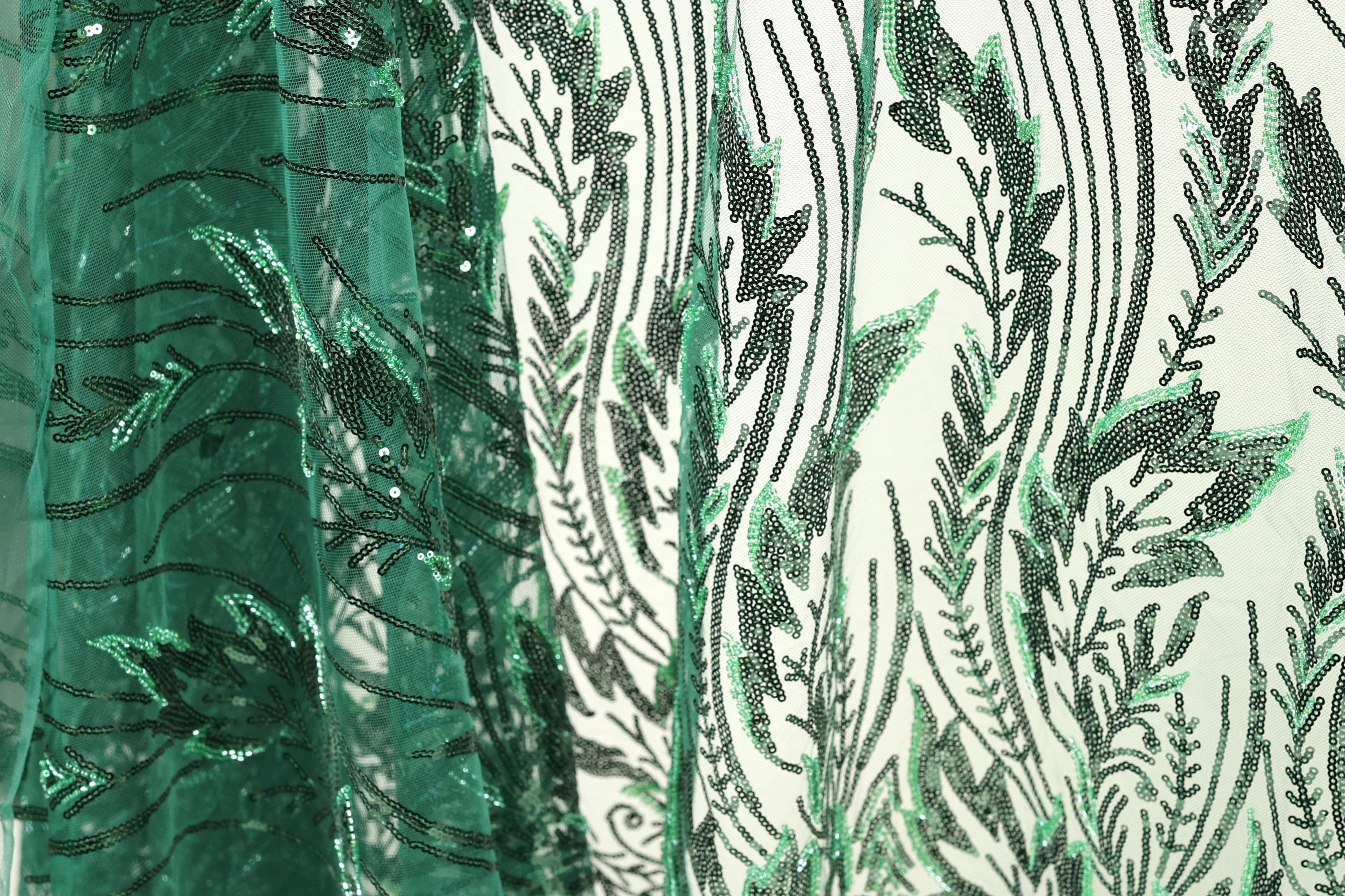 a close-up view of a fabric with a green and black leaf pattern. The fabric appears to be made of a sheer material, with a repeating pattern of green leaves and black lines. The leaves are arranged in a vertical orientation, creating a sense of depth and texture in the image.