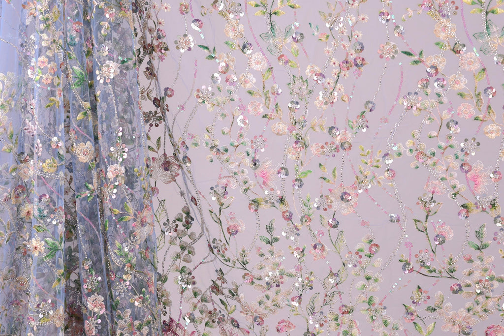 a close-up view of a fabric with a floral pattern, including various shades of pink, green, and white flowers and leaves. The fabric appears to be made of a sheer material, giving it a delicate and airy appearance. The pattern is intricate and detailed, with the flowers and leaves arranged in a way that creates a visually appealing and textured design.
