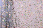 a close-up view of a fabric with a floral pattern, including various shades of pink, green, and white flowers and leaves. The fabric appears to be made of a sheer material, giving it a delicate and airy appearance. The pattern is intricate and detailed, with the flowers and leaves arranged in a way that creates a visually appealing and textured design.