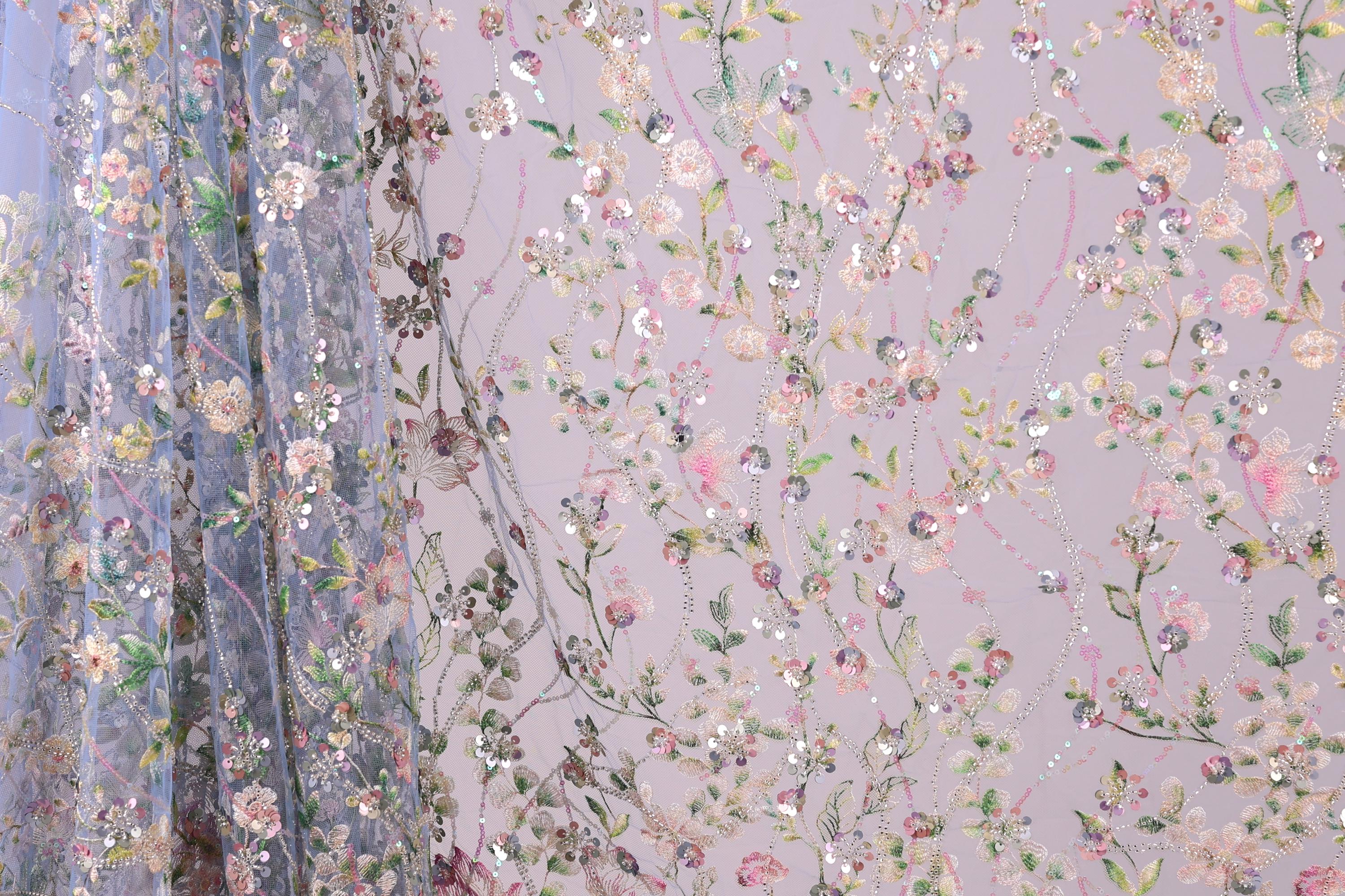 a close-up view of a fabric with a floral pattern, including various shades of pink, green, and white flowers and leaves. The fabric appears to be made of a sheer material, giving it a delicate and airy appearance. The pattern is intricate and detailed, with the flowers and leaves arranged in a way that creates a visually appealing and textured design.