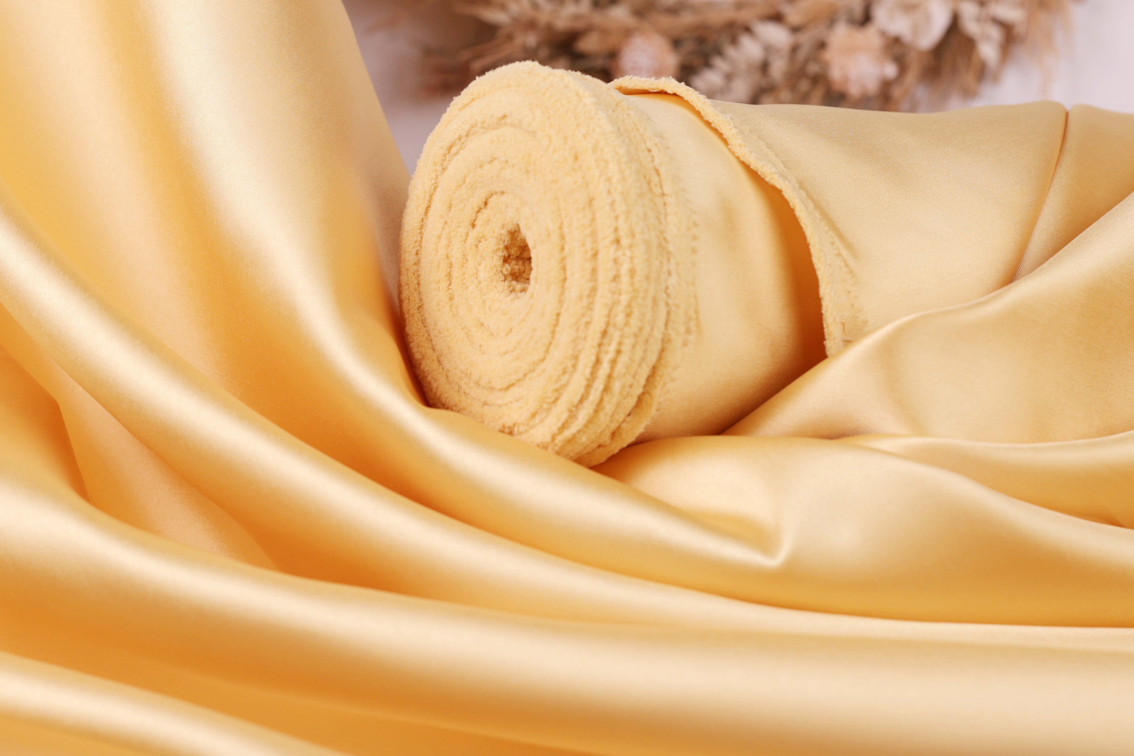 A close-up view of a yellow satin fabric, possibly silk, with a curled and folded appearance.