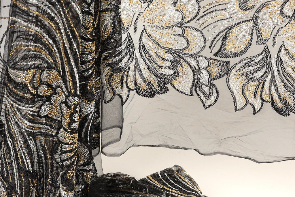 a close-up view of a black and gold sequined fabric with a floral pattern. The fabric appears to be a sheer material, with a black and gold color scheme. The image does not contain any text or other discernible objects or actions.