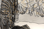 a close-up view of a black and gold sequined fabric with a floral pattern. The fabric appears to be a sheer material, with a black and gold color scheme. The image does not contain any text or other discernible objects or actions.