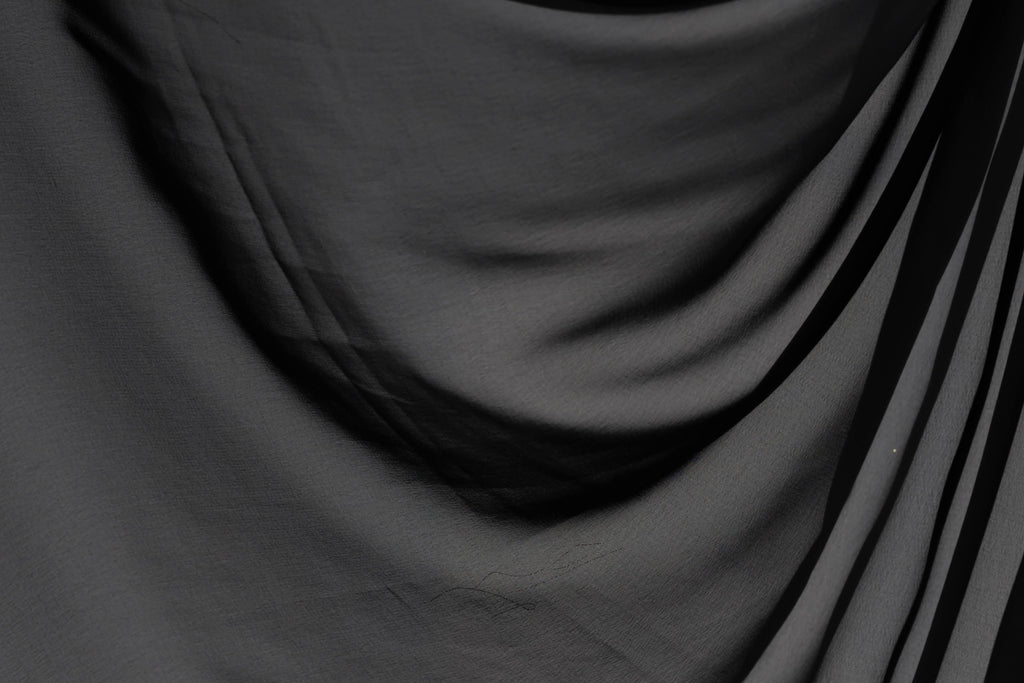 The image is a close-up of a black fabric, possibly a piece of clothing or a textile. The fabric appears to be wrinkled and has a textured surface, giving it a somewhat rough appearance.