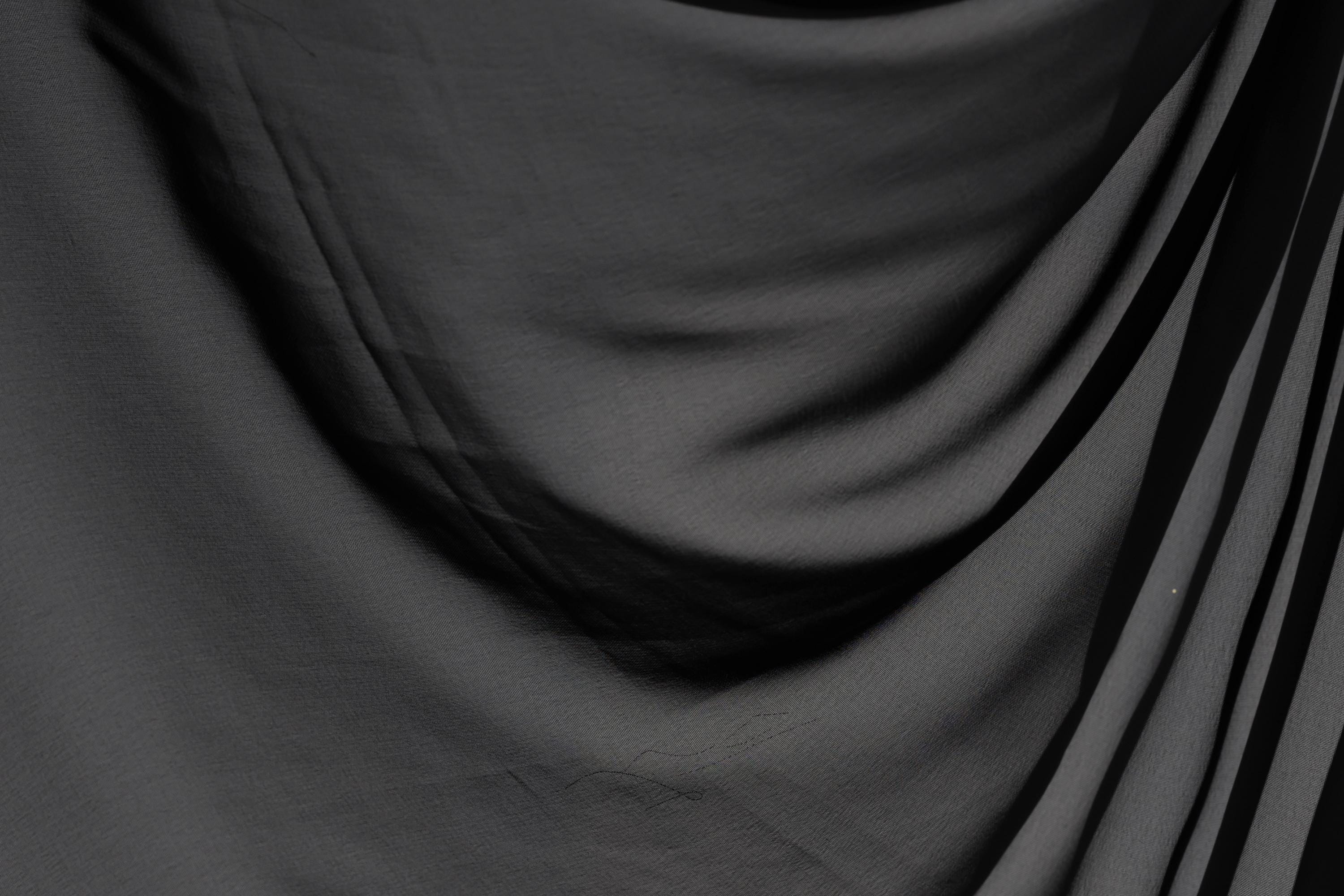 The image is a close-up of a black fabric, possibly a piece of clothing or a textile. The fabric appears to be wrinkled and has a textured surface, giving it a somewhat rough appearance.