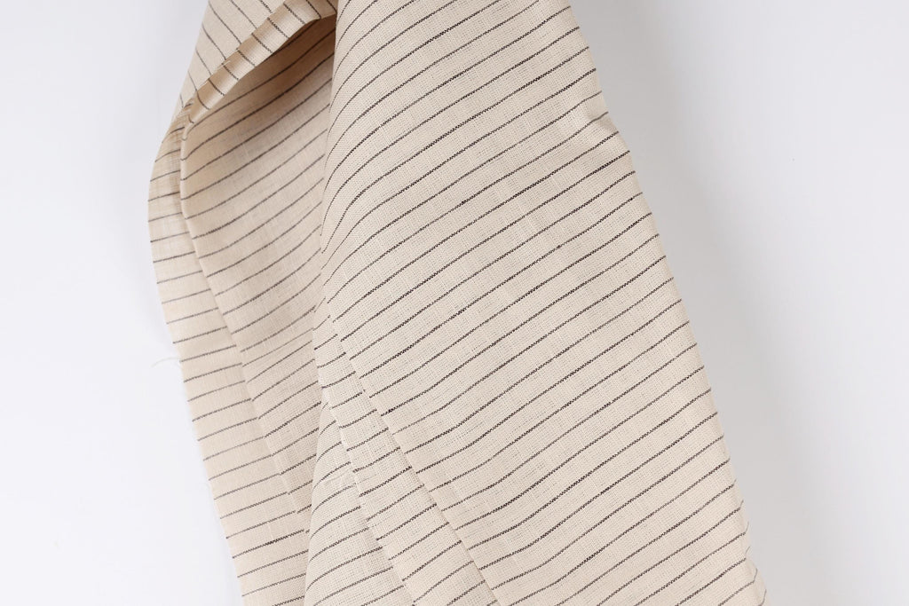 A close-up view of a beige fabric with black stripes, hanging against a white background.