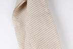 A close-up view of a beige fabric with black stripes, hanging against a white background.