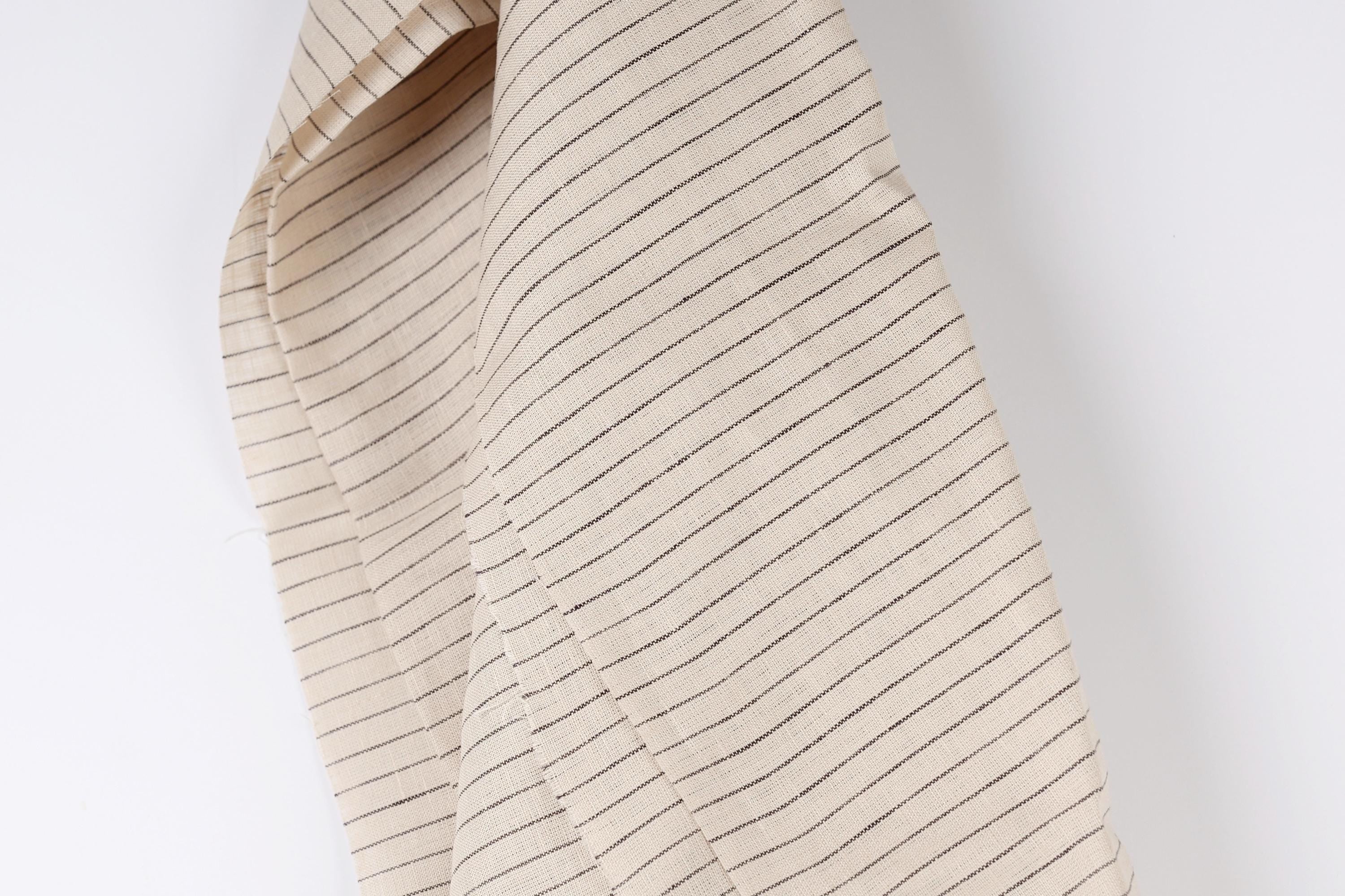 A close-up view of a beige fabric with black stripes, hanging against a white background.