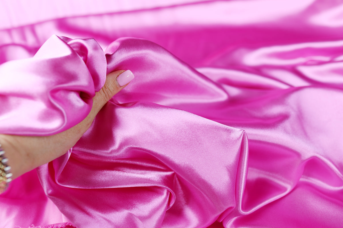 A hand is holding a piece of pink satin fabric, which appears to be soft and smooth.