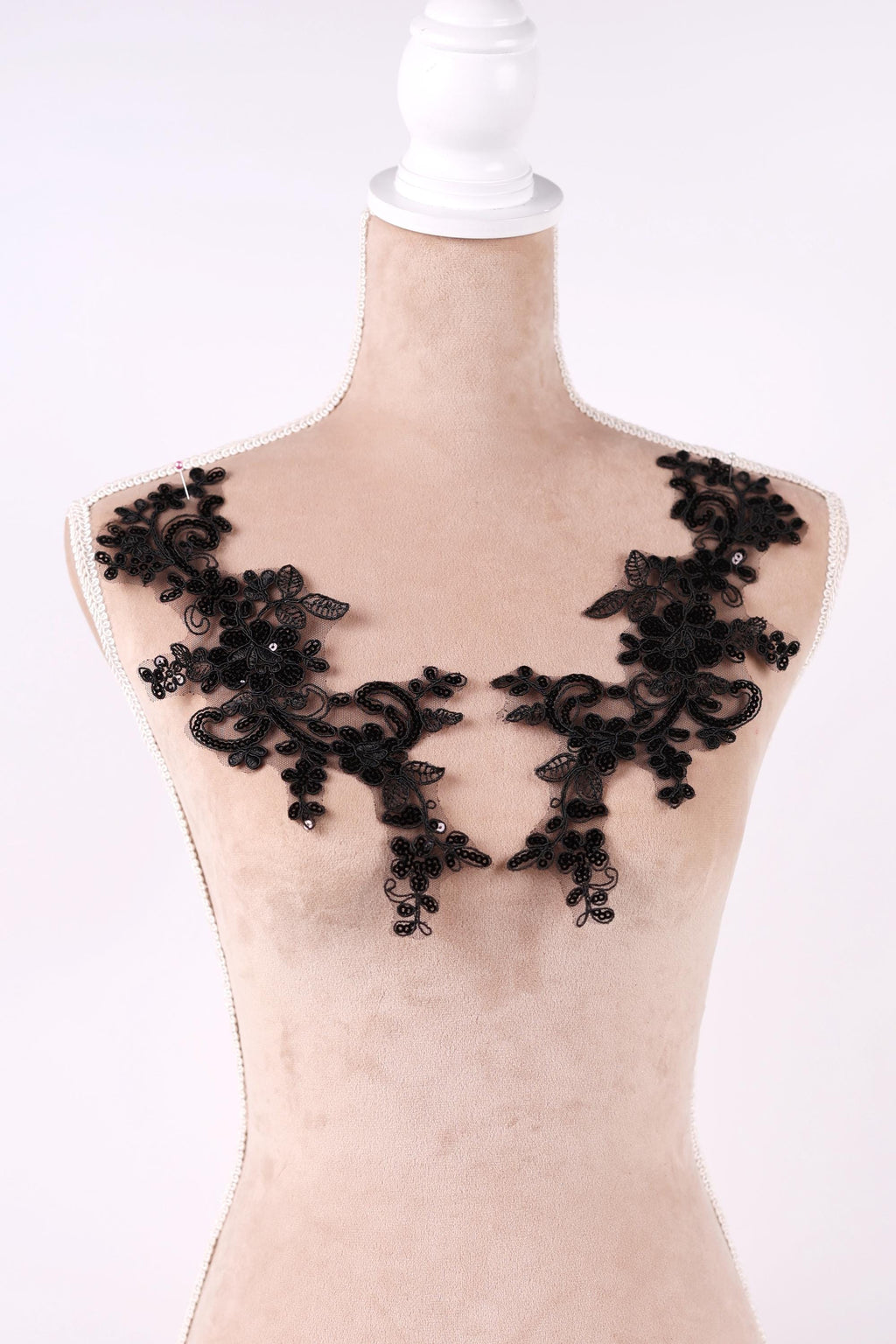 A mannequin wearing a beige dress with black lace appliques on the shoulders.