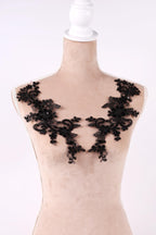 A mannequin wearing a beige dress with black lace appliques on the shoulders.