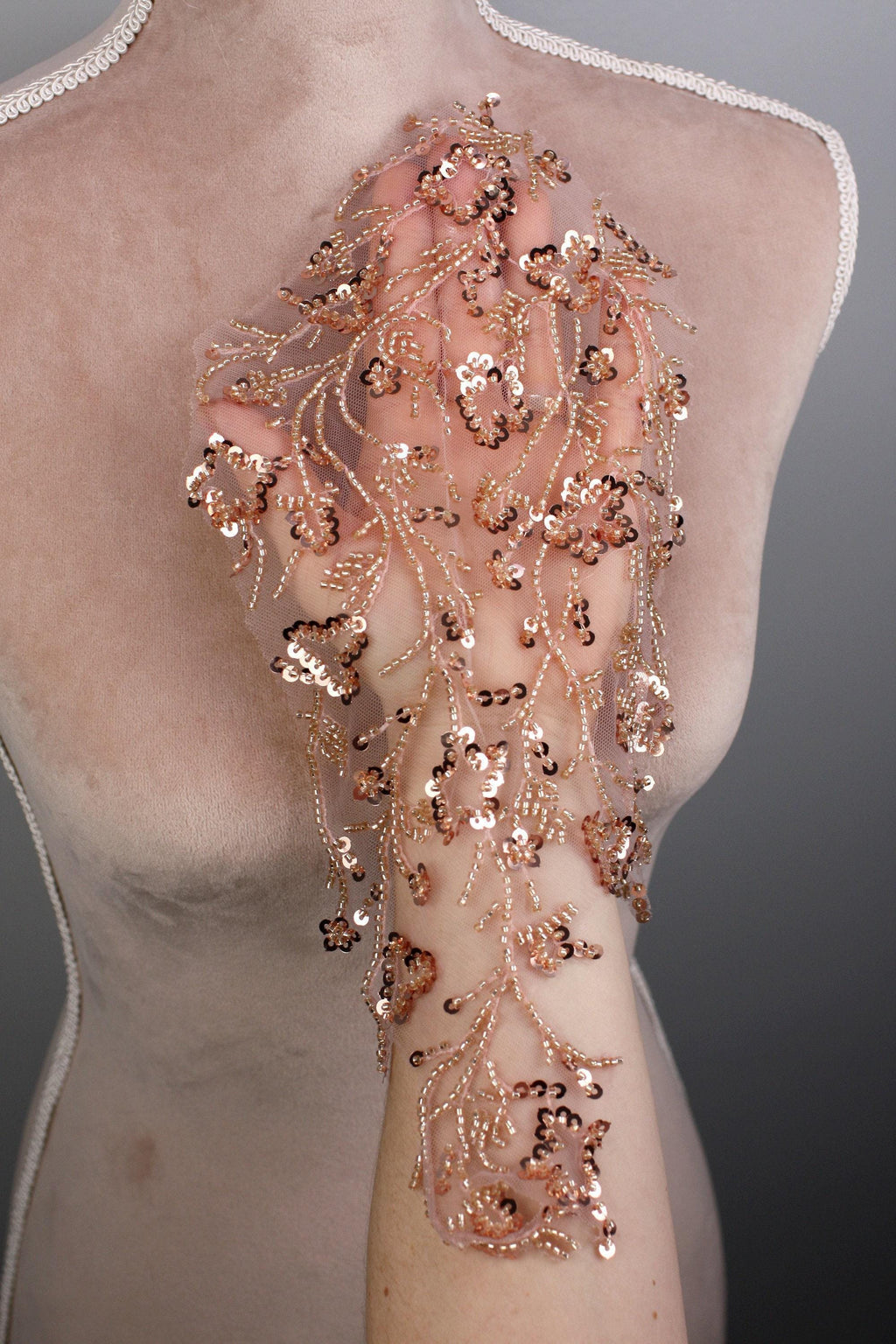 a mannequin with a delicate, intricate beaded sleeve. The sleeve is adorned with a floral pattern of small, gold-colored beads that create a visually striking and elegant design.
