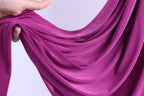 A hand is holding a piece of purple fabric, which appears to be a flowing, draped garment.