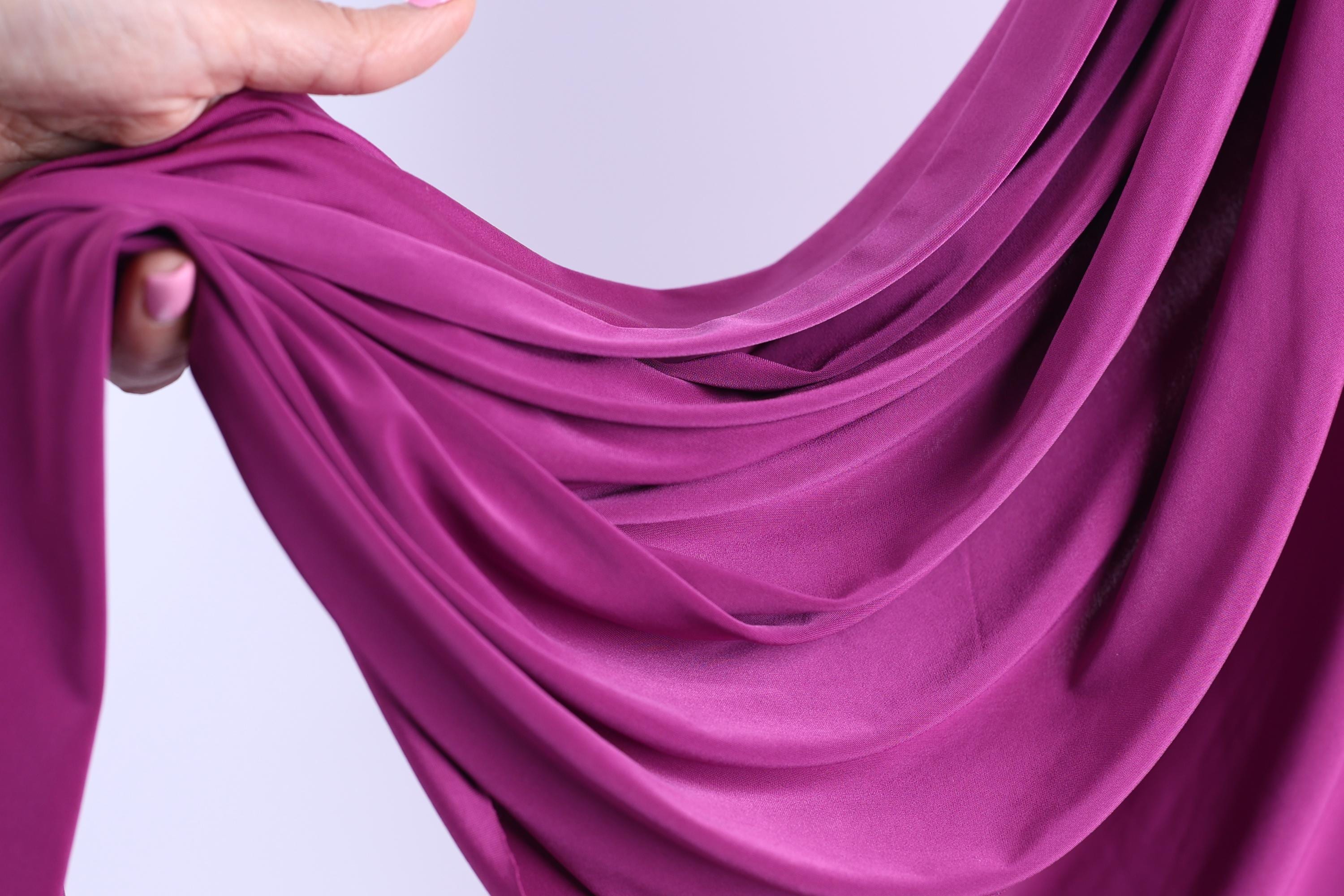 A hand is holding a piece of purple fabric, which appears to be a flowing, draped garment.