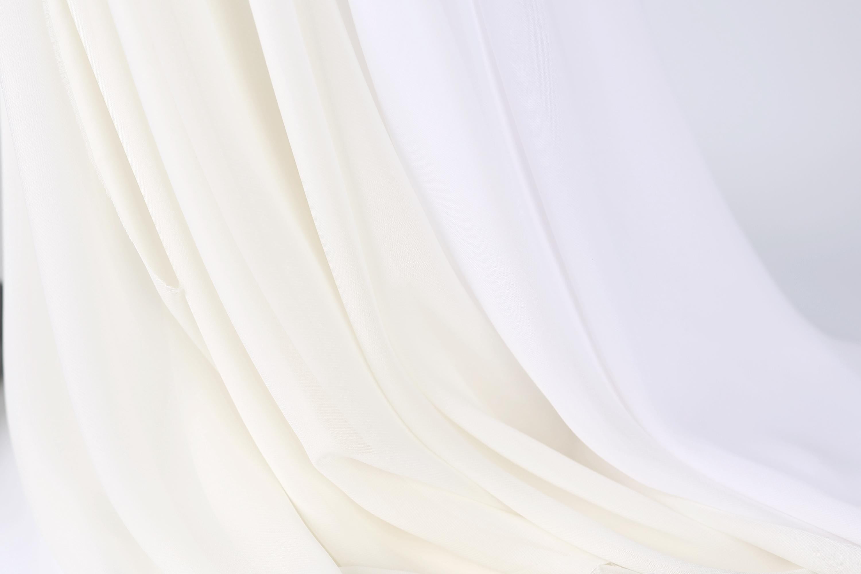 The image is a close-up of a white fabric, possibly a sheer or sheer-like material, with a soft, flowing texture.