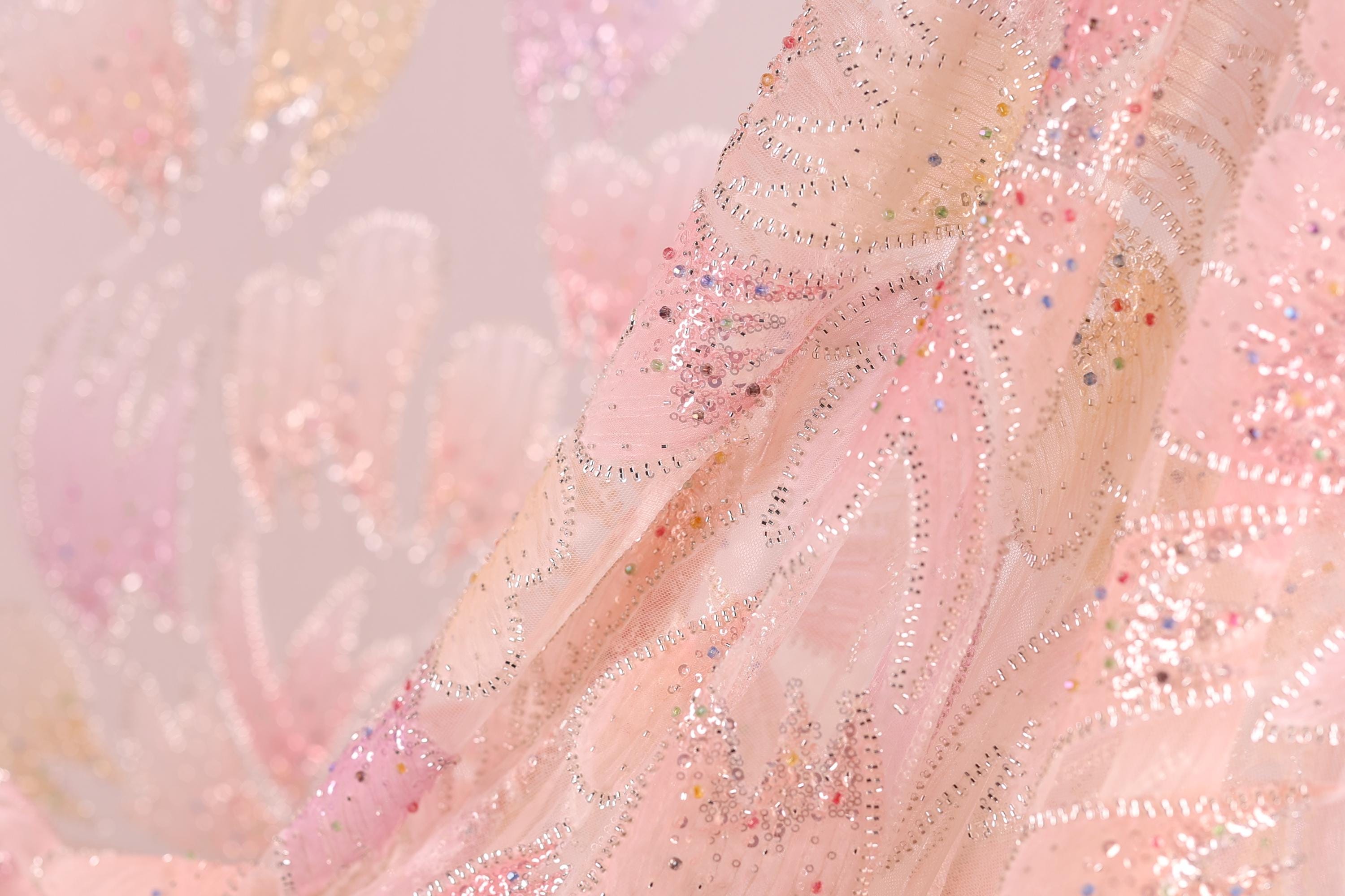 The image is a close-up of a fabric with a pink and white floral pattern, featuring small sequins or beads that add texture and sparkle to the fabric.