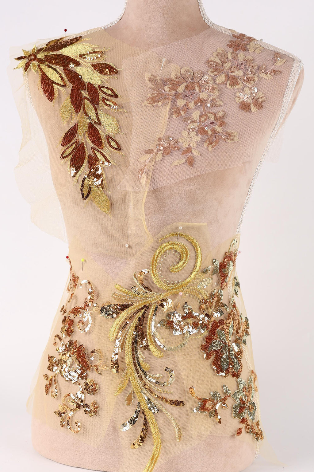 a delicate, intricately embroidered dress with a floral pattern. The dress is adorned with gold and brown sequins, creating a visually striking and elegant design.