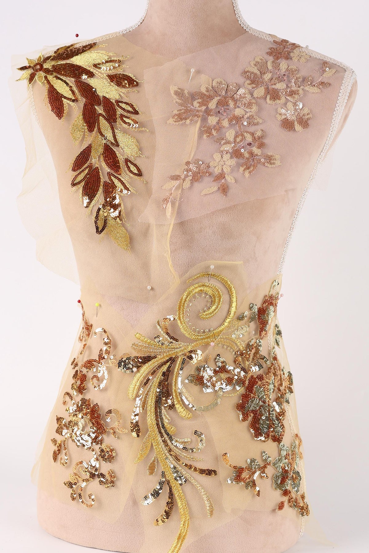 a delicate, intricately embroidered dress with a floral pattern. The dress is adorned with gold and brown sequins, creating a visually striking and elegant design.