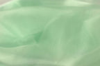 A close-up view of a soft, mint green fabric, possibly silk or chiffon, with a slightly wrinkled texture.