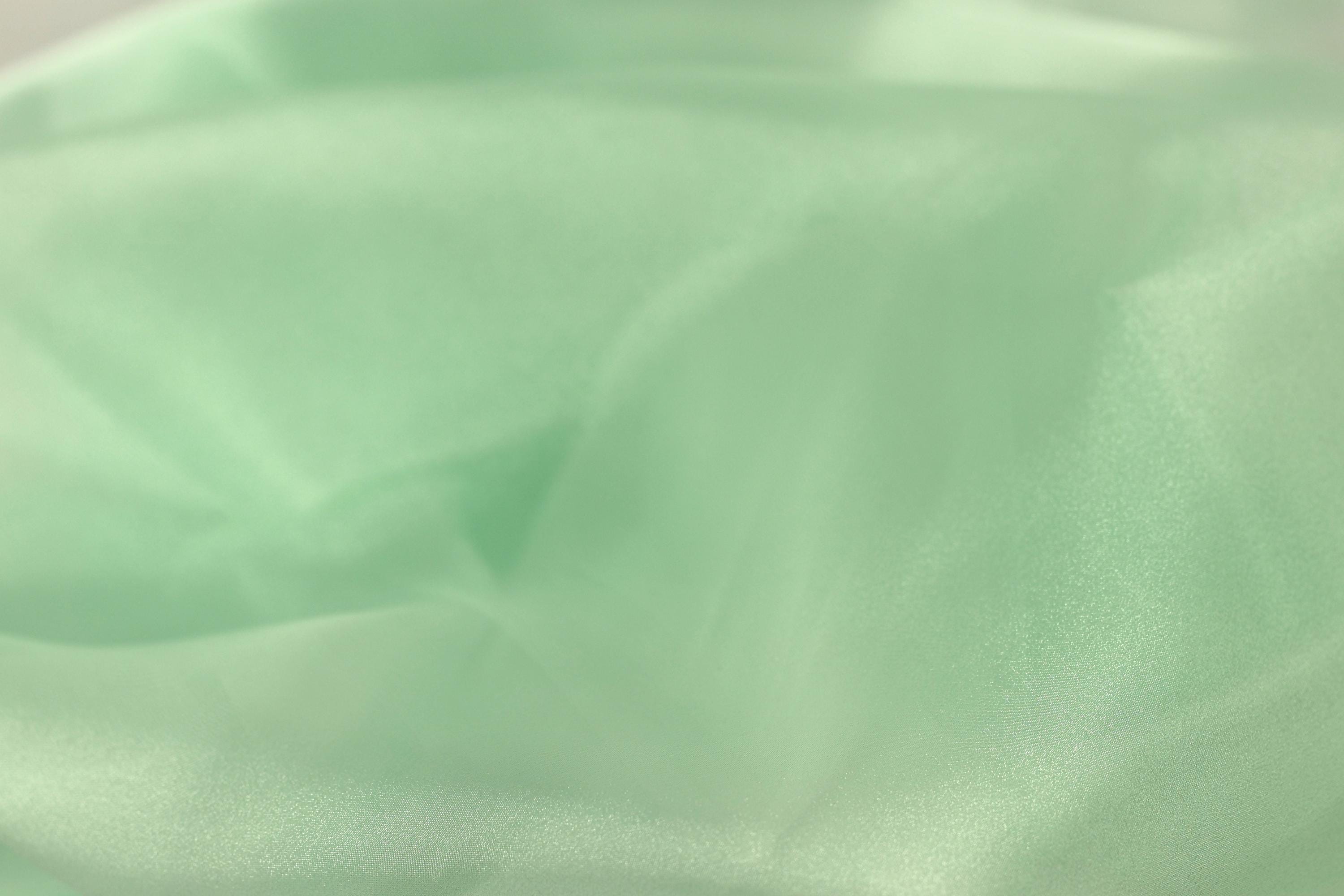 A close-up view of a soft, mint green fabric, possibly silk or chiffon, with a slightly wrinkled texture.