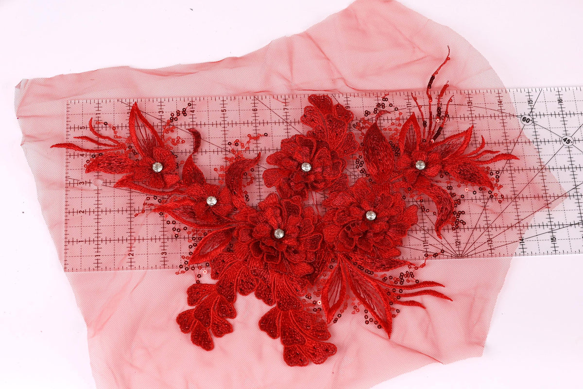 a close-up view of a red floral embroidery on a pink fabric, with a ruler placed over it to measure the size.