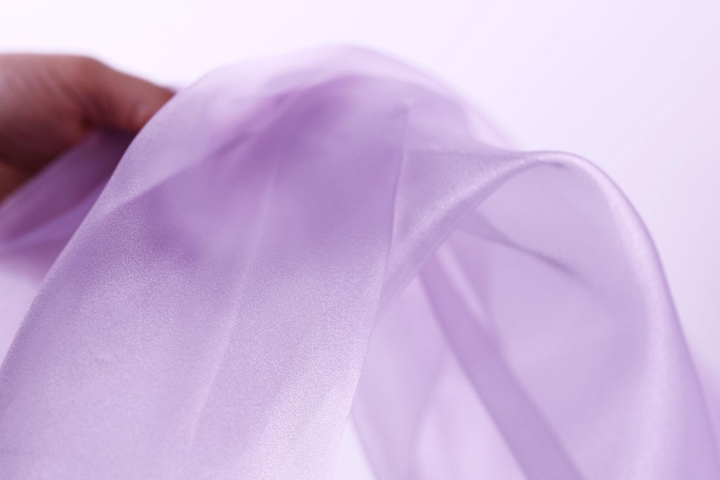 A hand is holding a piece of lavender-colored fabric, which appears to be a soft, flowing material.