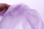 A hand is holding a piece of lavender-colored fabric, which appears to be a soft, flowing material.
