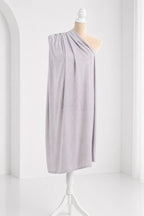 A mannequin wearing a gray draped garment stands on a white stand against a white background.