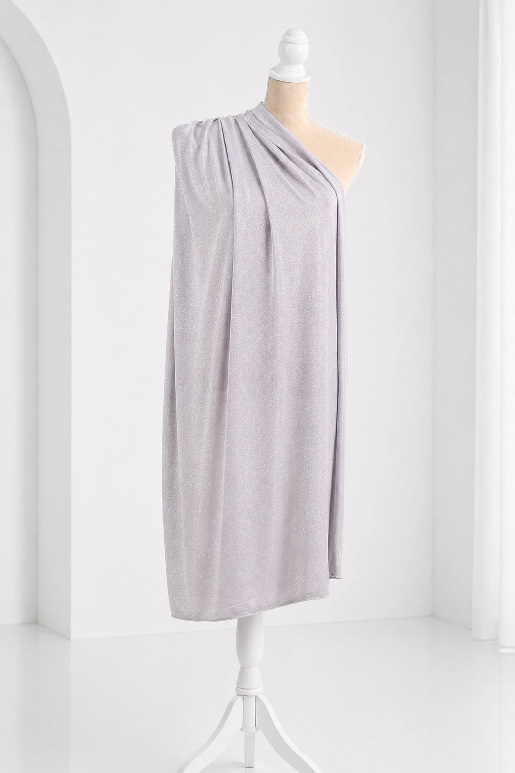 A mannequin wearing a gray draped garment stands on a white stand against a white background.