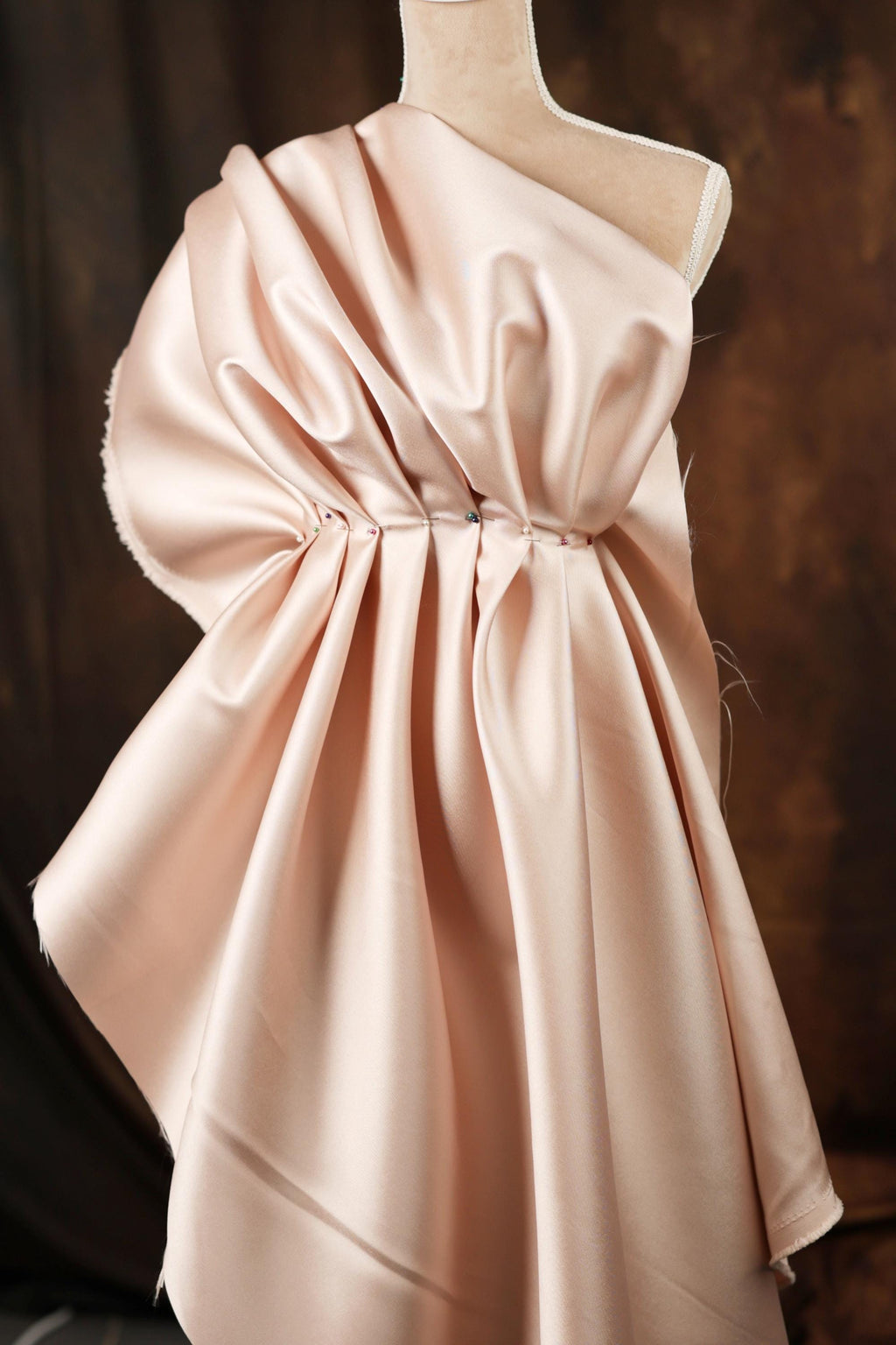 A mannequin wearing a pink satin dress with a draped, flowing silhouette.
