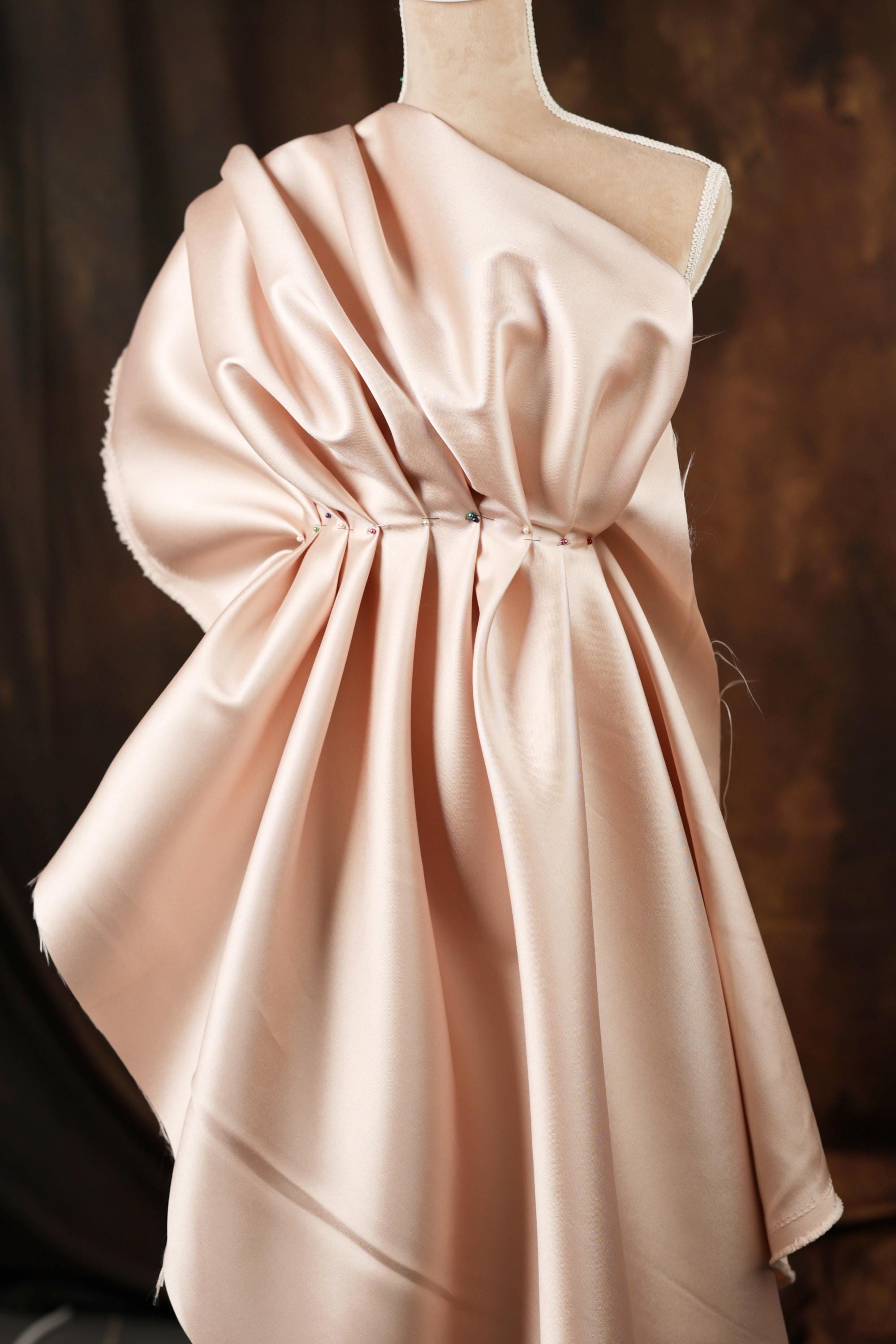 A mannequin wearing a pink satin dress with a draped, flowing silhouette.