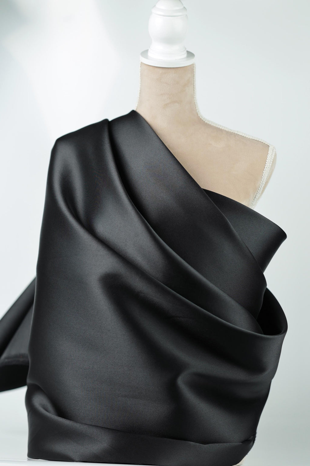 A mannequin wearing a black satin fabric draped over its body.