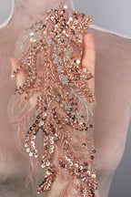 A hand is holding a piece of fabric with a delicate, intricate design of sequins and lace.