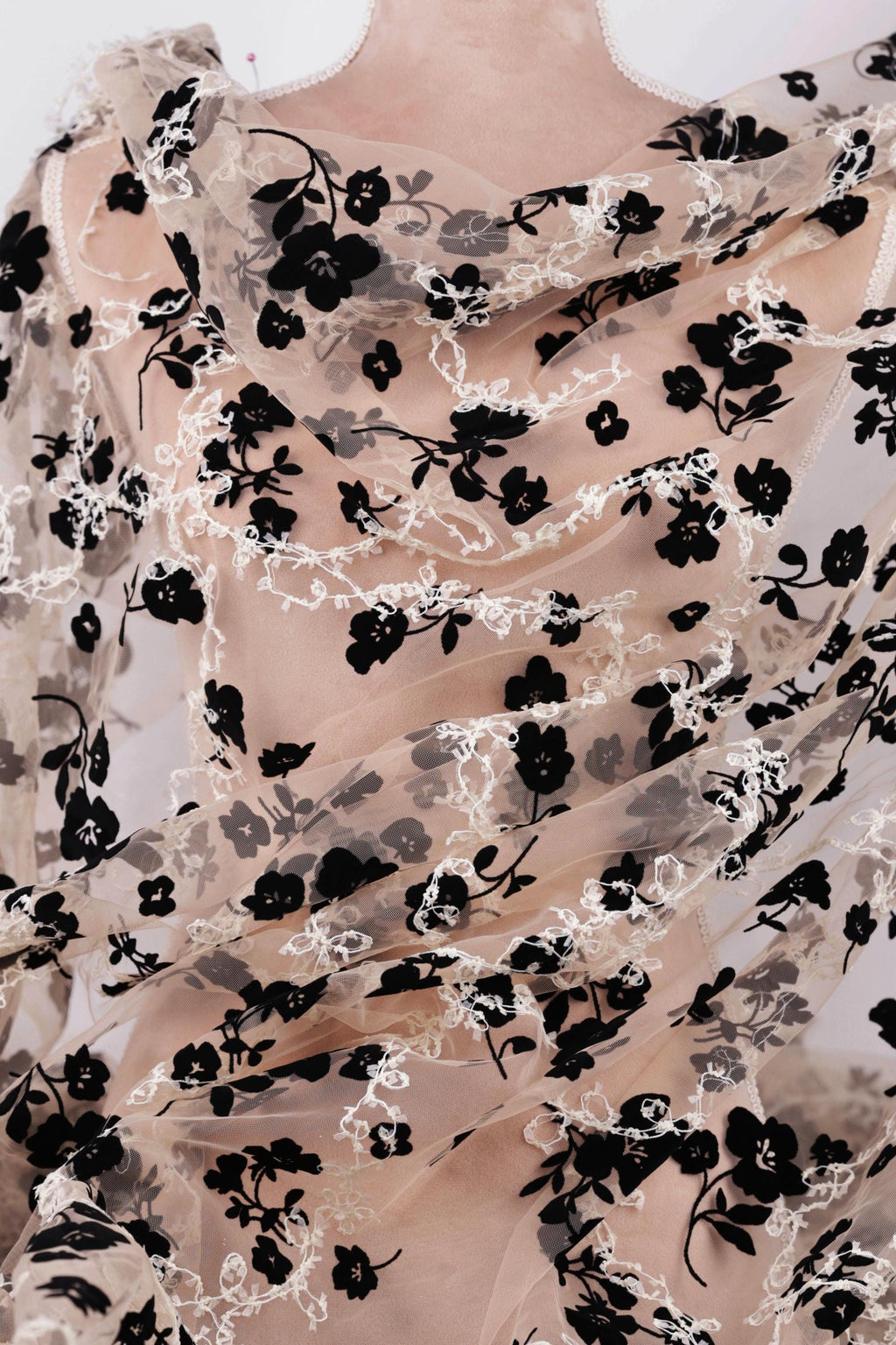 a close-up view of a sheer fabric with a black floral pattern. The fabric appears to be made of sheer material, giving it a delicate and airy appearance. The black flowers are arranged in a way that covers the entire fabric, creating a visually striking contrast against the lighter background.