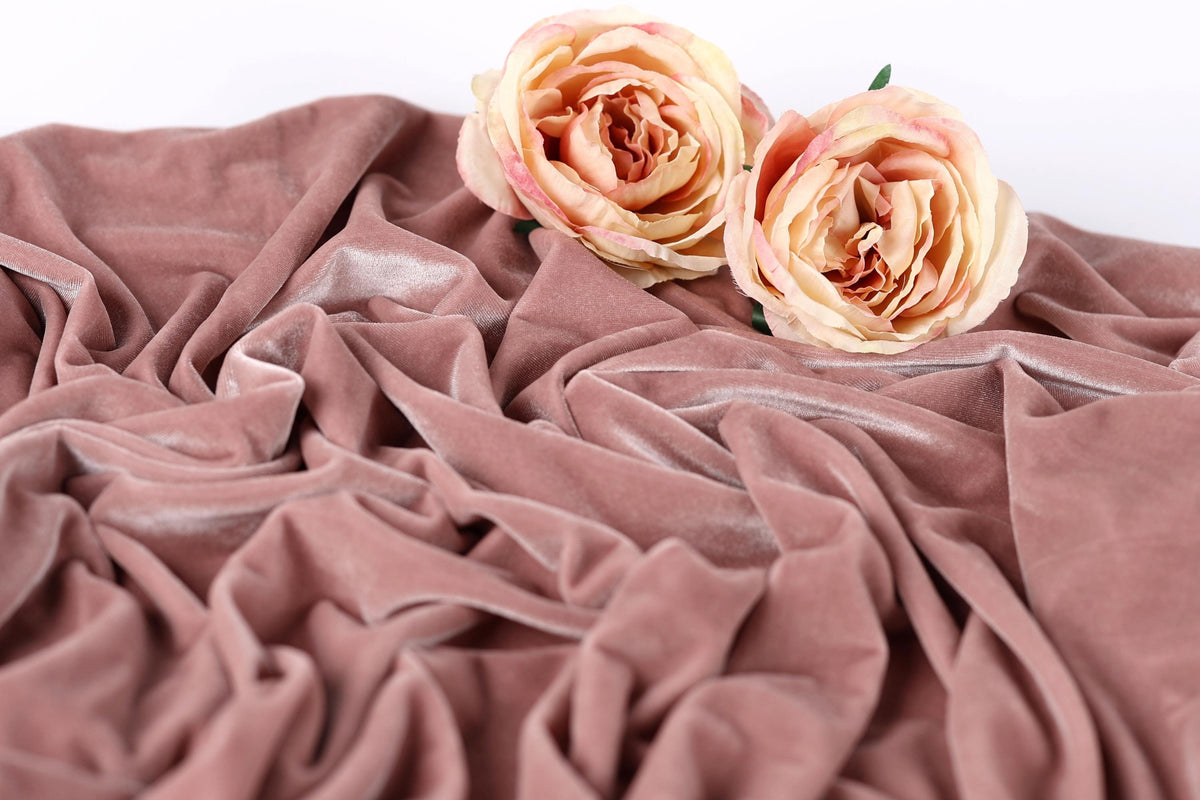 Two light pink roses resting on a crumpled pink velvet fabric.
