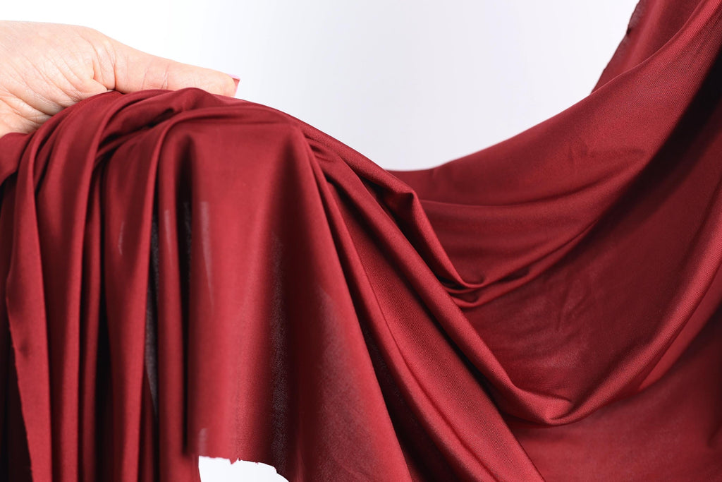 A hand is holding a red fabric, which appears to be a type of chiffon or sheer material. The fabric is folded and draped in a way that it covers a significant portion of the hand.