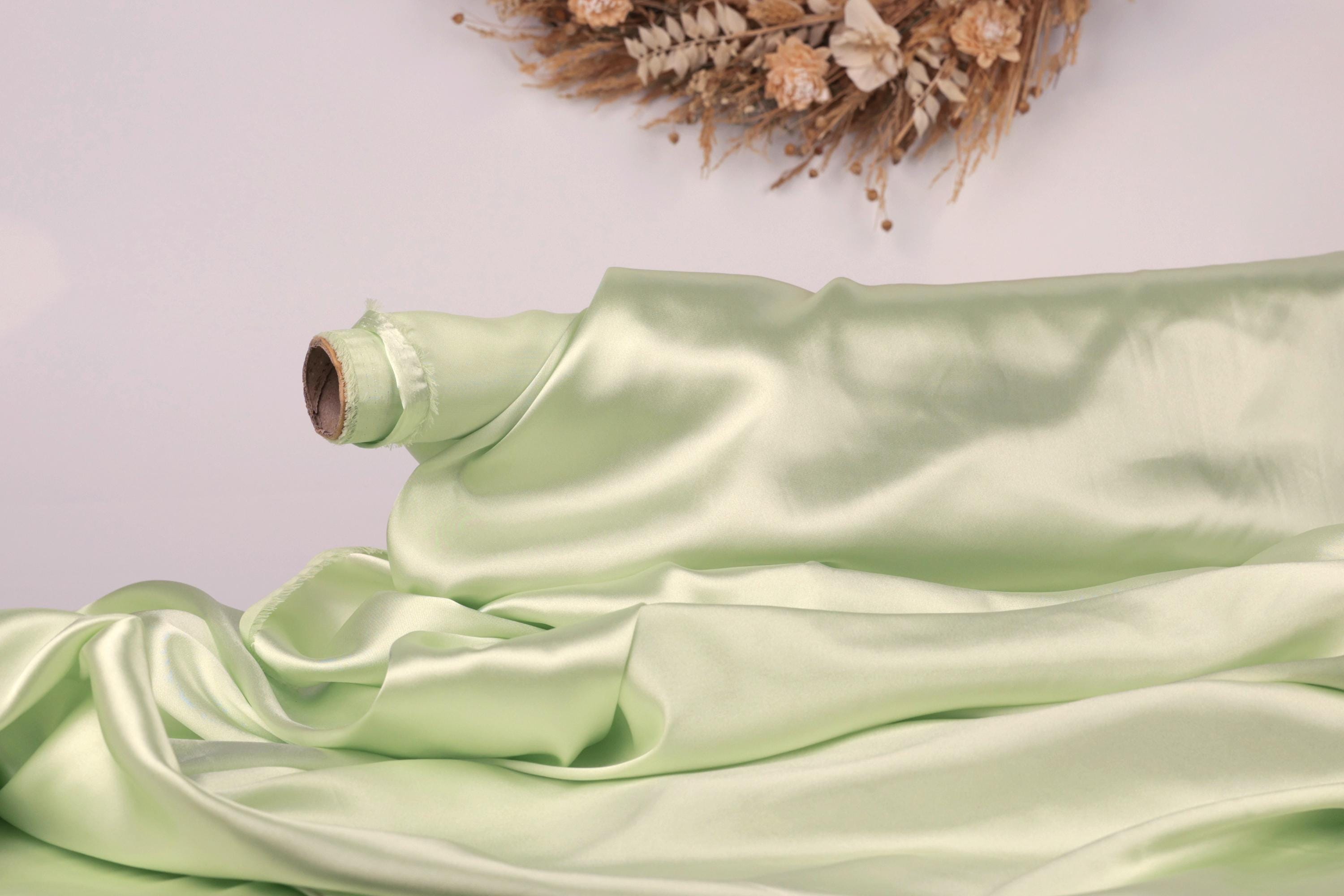 A roll of pale green satin fabric is draped over a surface, with a wreath of dried flowers hanging on the wall behind it.