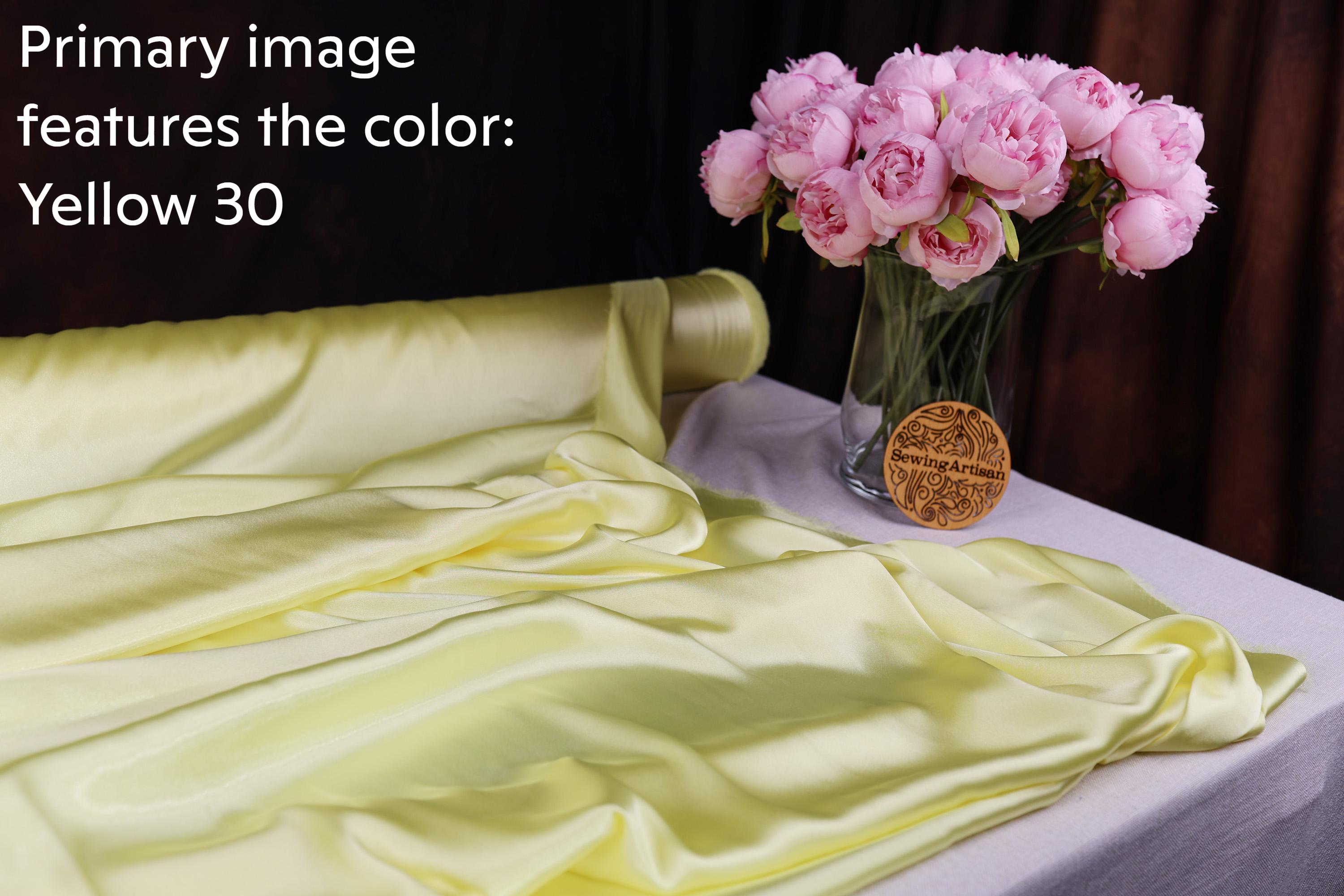 a bouquet of pink roses in a glass vase, placed on a table with a yellow fabric draped over it.