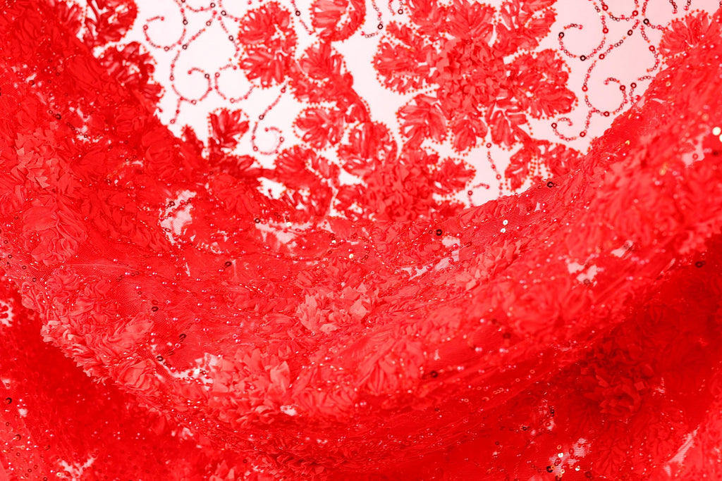 The image is a close-up of a red fabric with a floral pattern, featuring a lot of red sequins and a shiny texture.