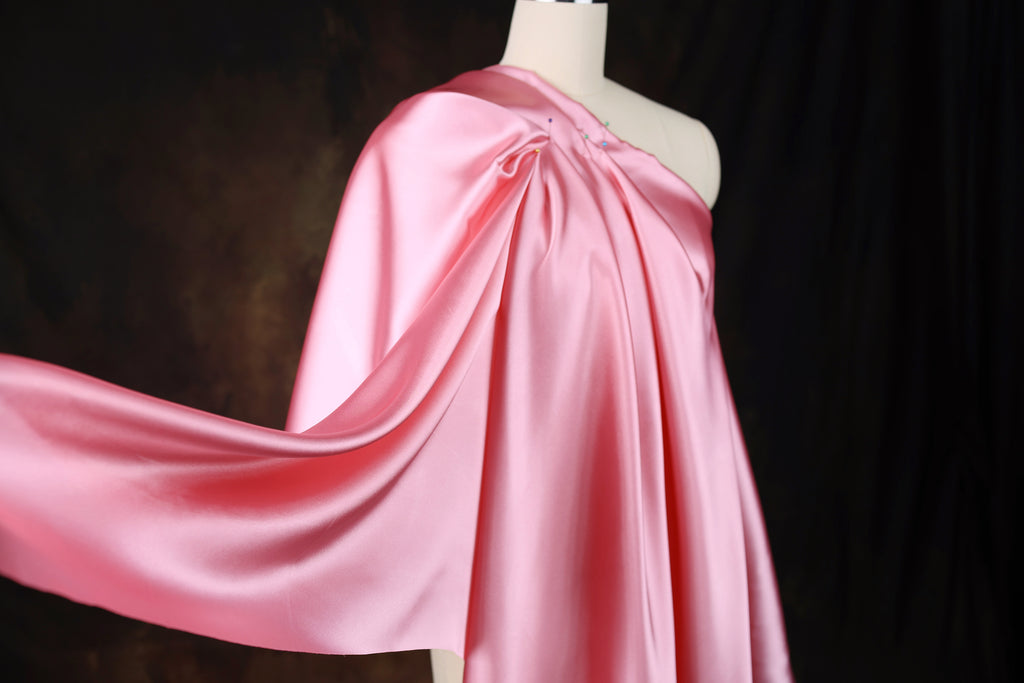 A mannequin wearing a pink satin one-shoulder dress with a flowing, draped design.