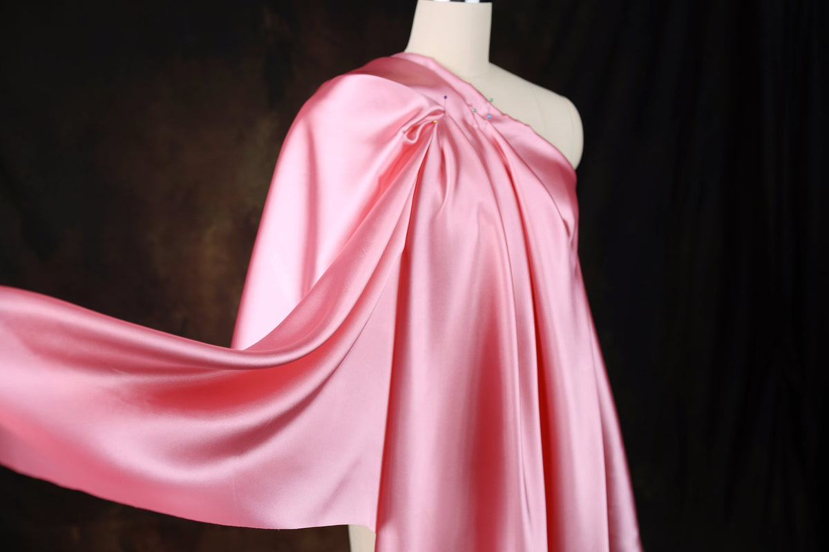 A mannequin wearing a pink satin one-shoulder dress with a flowing, draped design.