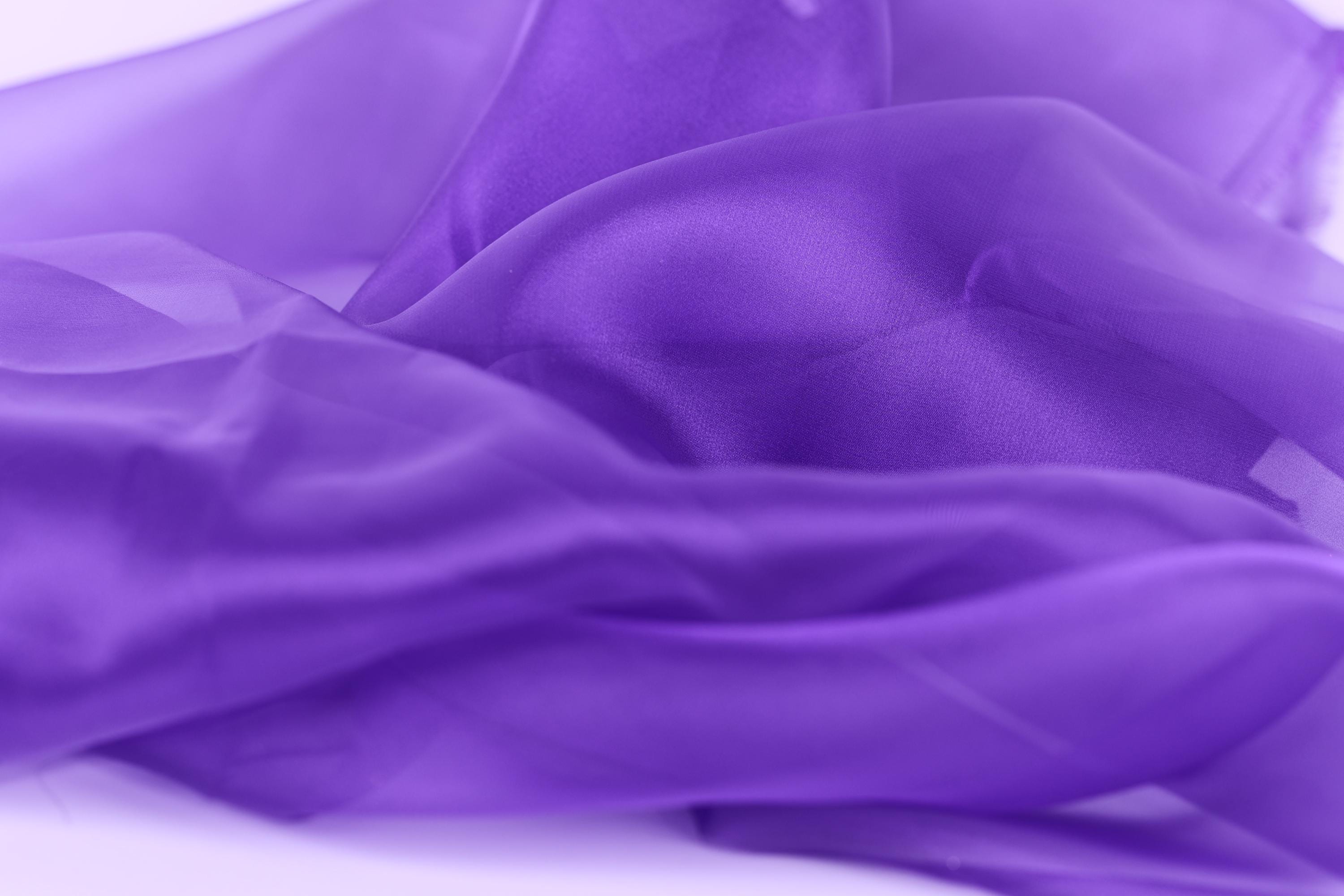 The image is a close-up of a soft, flowing purple fabric, possibly silk or chiffon, with a slightly wrinkled texture.