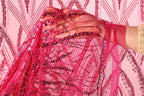 A hand is holding a pink sequin fabric, with the fabric's intricate patterns and designs visible.