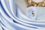 A close-up view of a blue satin fabric, with a rolled-up piece of the fabric visible in the background.