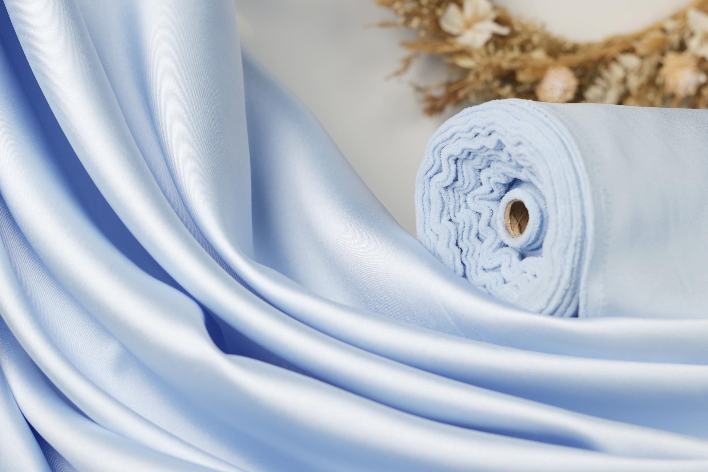 A close-up view of a blue satin fabric, with a rolled-up piece of the fabric visible in the background.